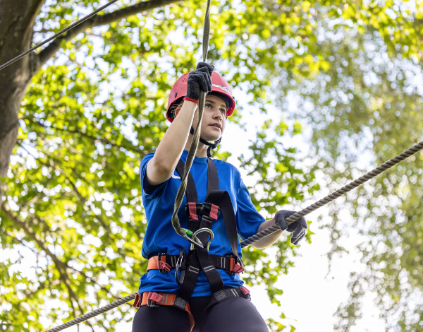 Eine Jugendliche in Kletterausrstung balanciert konzentriert an einem Seil