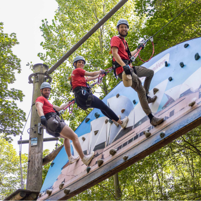 Drei junge Leute schauen lachend von der Boulderwand in die Kamera