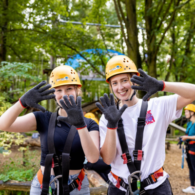 Zwei junge Frauen im Halbportrt in Kletterausrstung lachen in die Kamera
