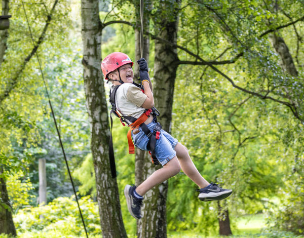 Junge mit Helm schwebt durch den Kletterpark und lacht in die Kamera