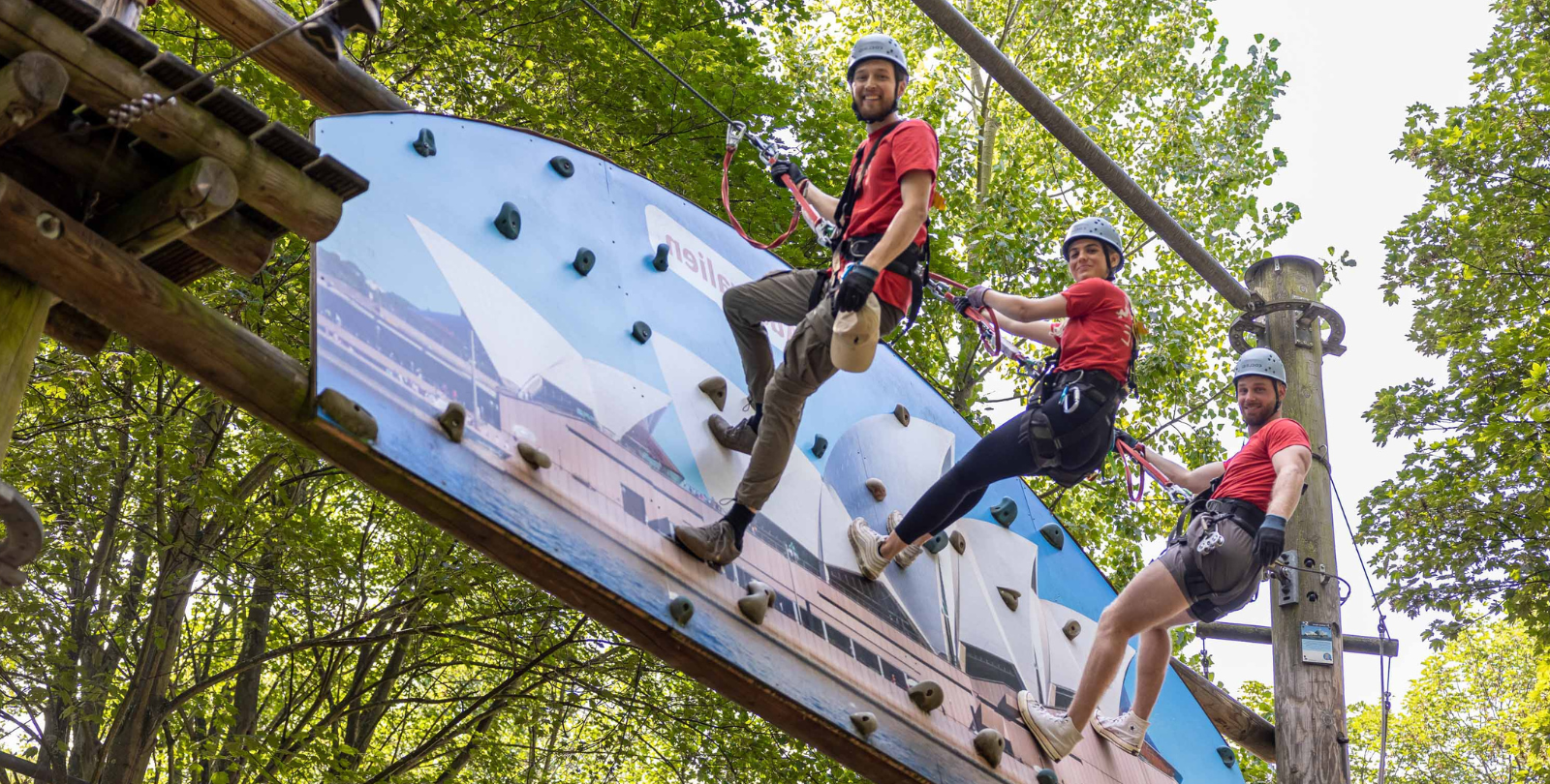 Drei Mitarbeiter stehen gesichert in einer Boulderwand und lcheln in die Kamera